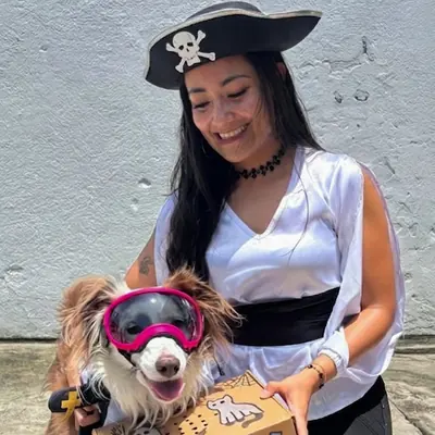 Una joven con sombrero pirata junto a un perro con gafas de disfraz.