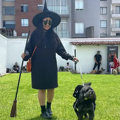 Una tutora disfrazada de bruja pasea a su perro negro por el jardín de la fiesta.
